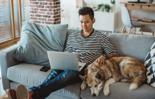 Young man sitting on the couch with his dog and using his laptop