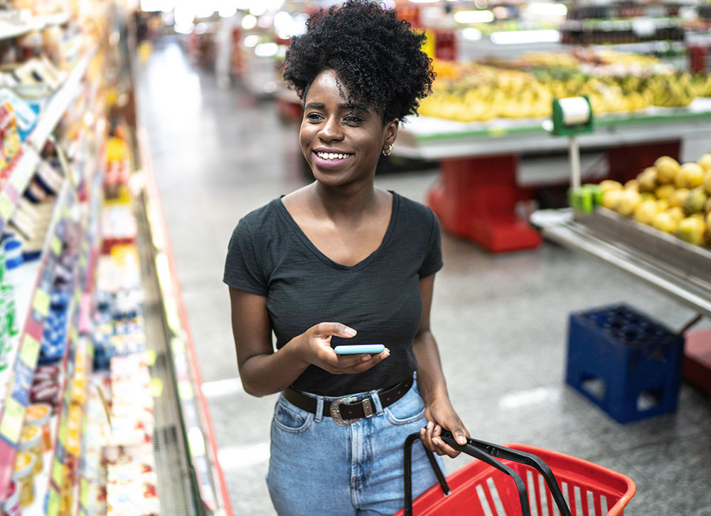 Young woman using mobile phone and choosing product in supermarket