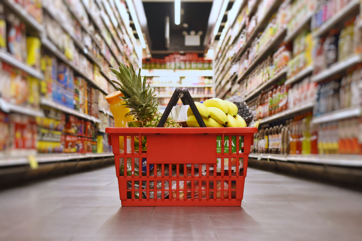 A grocery basket full of produce sitting on the floor of a grocery store.