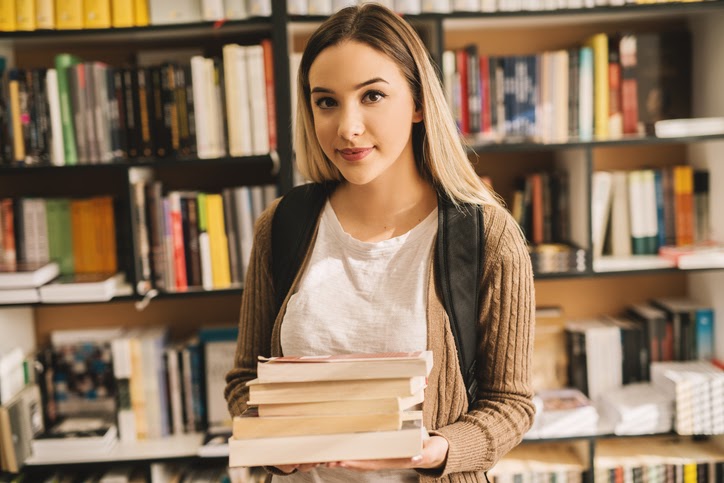 A young female student smiling while holding college textbooks in a bookstore.