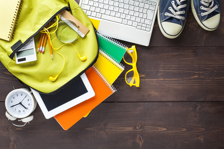 An open laptop surrounded by several college school supplies, including pencils, sticky notes, and a backpack.