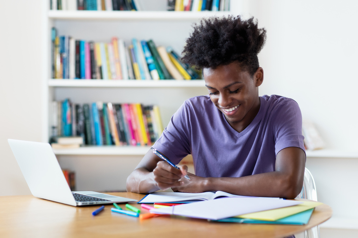 A young male student writing down notes in preparation for college.