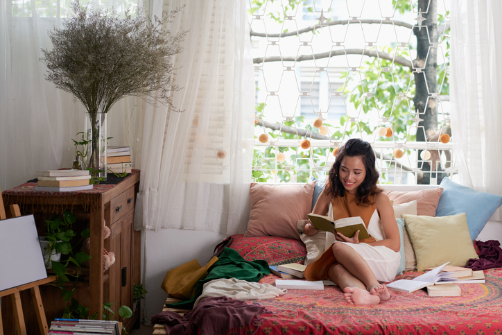 A smiling young woman reading in her decorated college apartment.