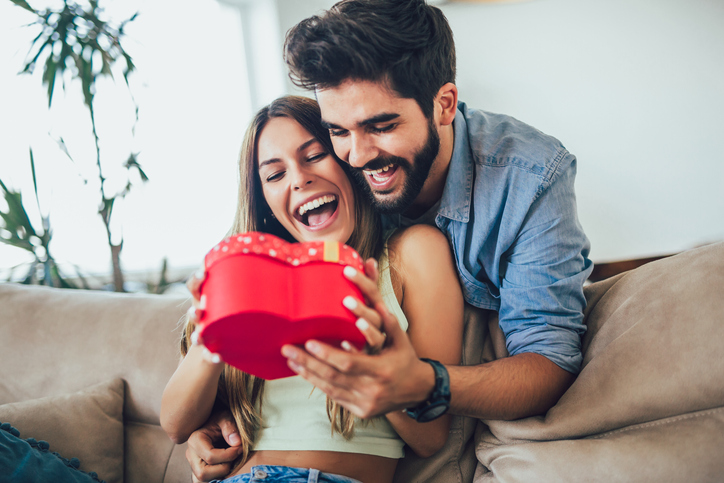 Happy couple with gift box hugging at home.